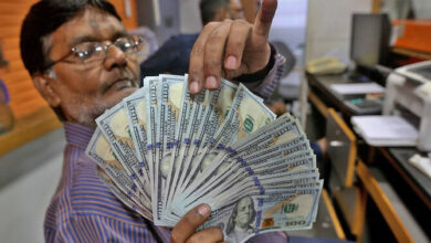 تاجر عملة باكستاني يفحص أوراق نقدية من فئة 100 دولار أمريكي في مكتب صرافة بكراتشي